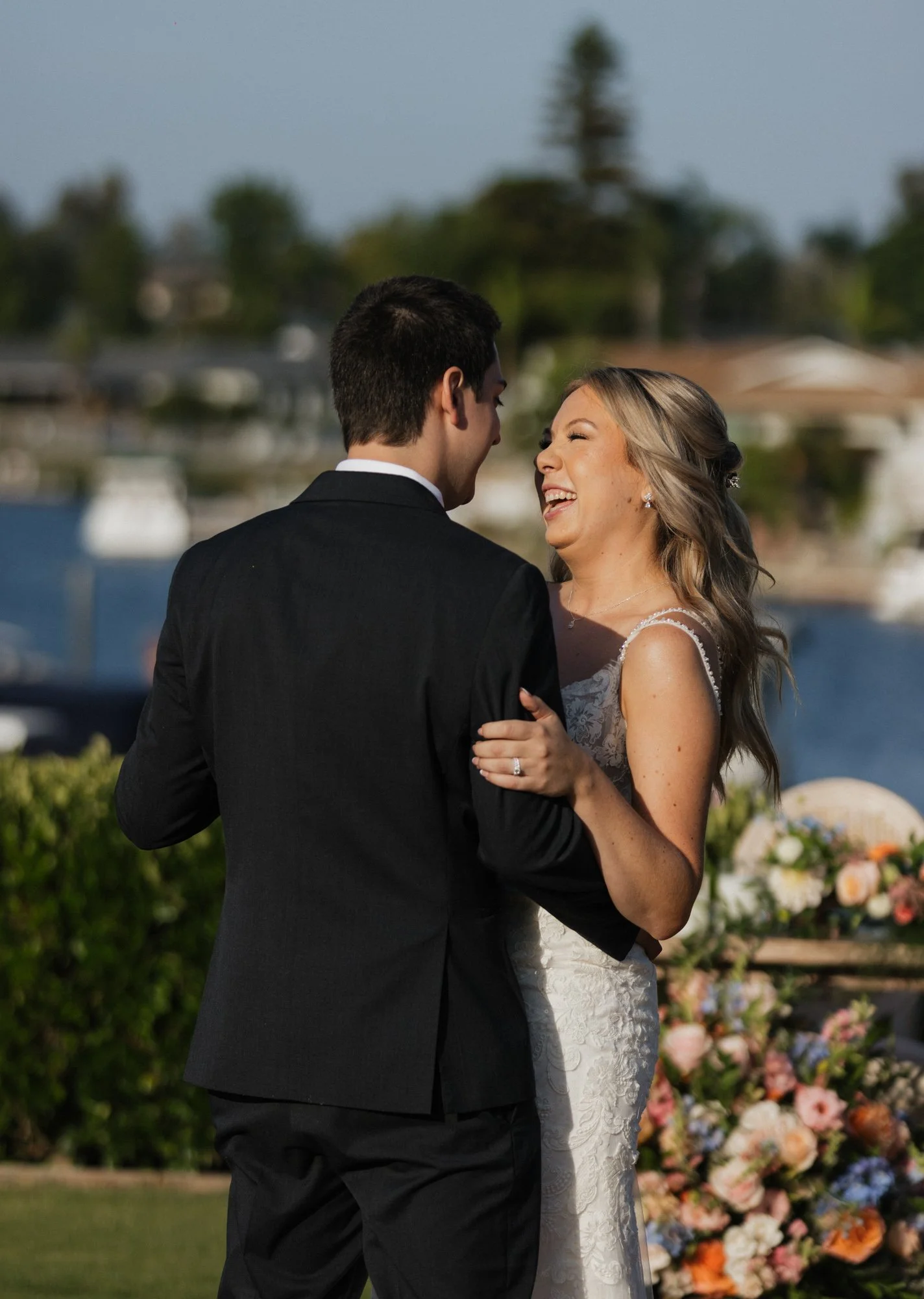 A bride and groom dancing outdoors at their wedding, with a large floral arrangement in the background at LakeHouse Resort wedding venue in Lake San Marcos.