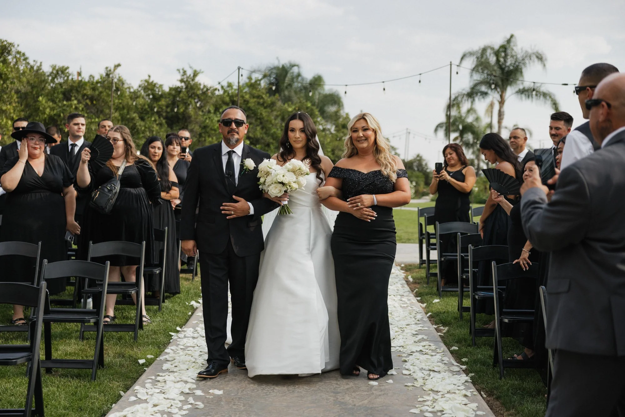 A candid photographer takes a candid photo of her as she walks with her parents down the aisle on her wedding day in Los Angeles California.