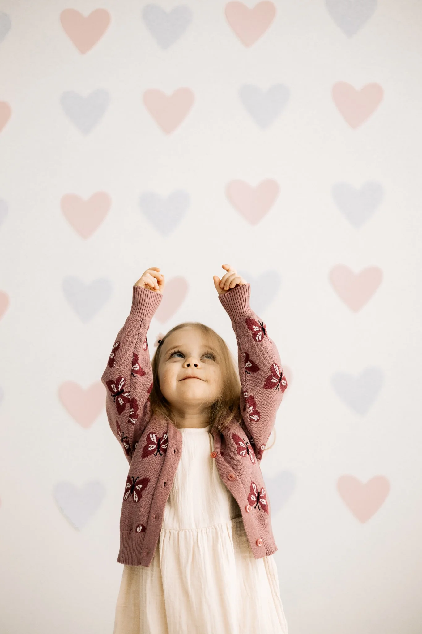 iloinen lapsi kurkottelee sydämiä yllään vaaleanpunainen perhoskuvioitu neule