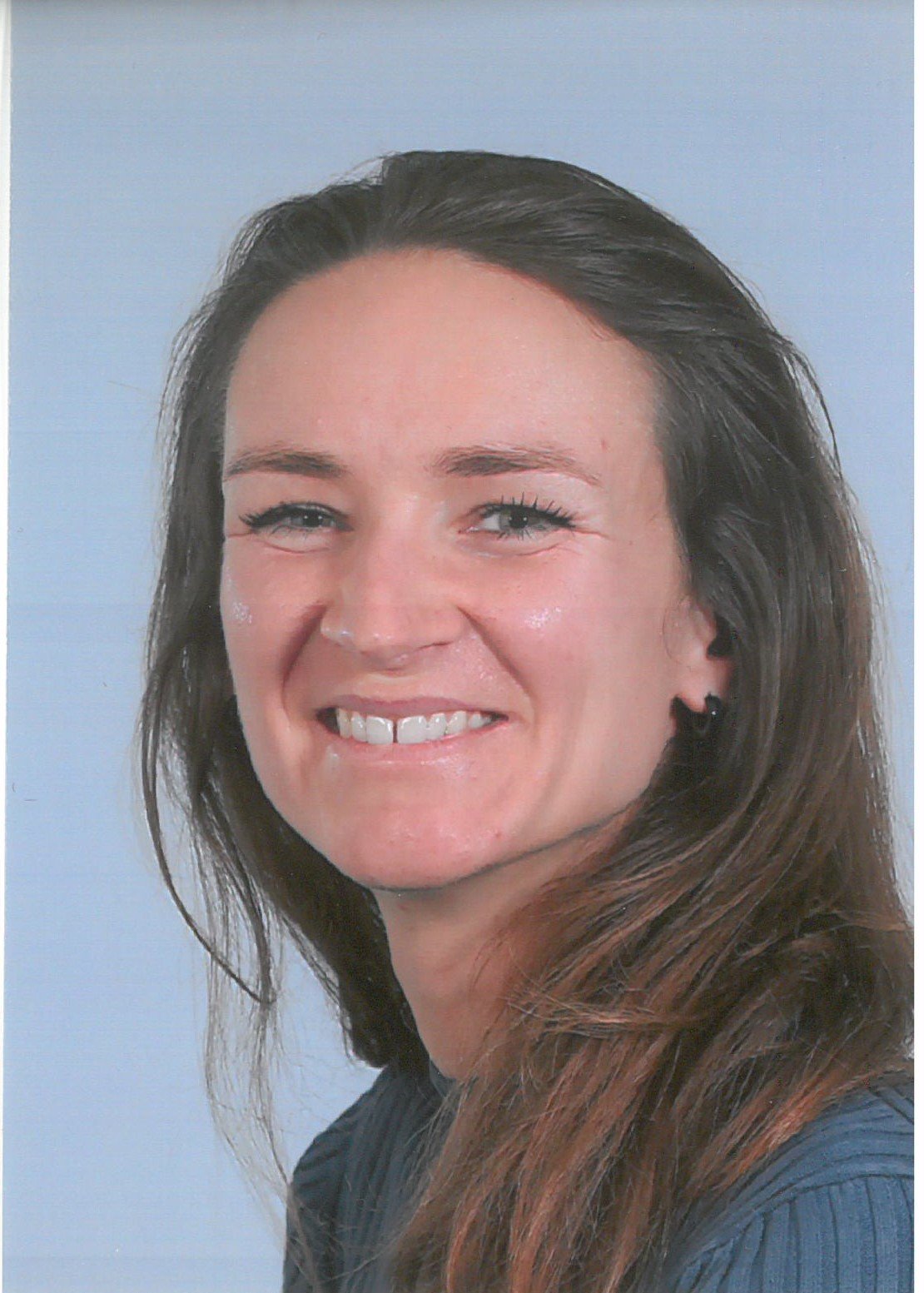 Portret van een glimlachende vrouw met bruin haar en lichte huid op een lichte achtergrond.