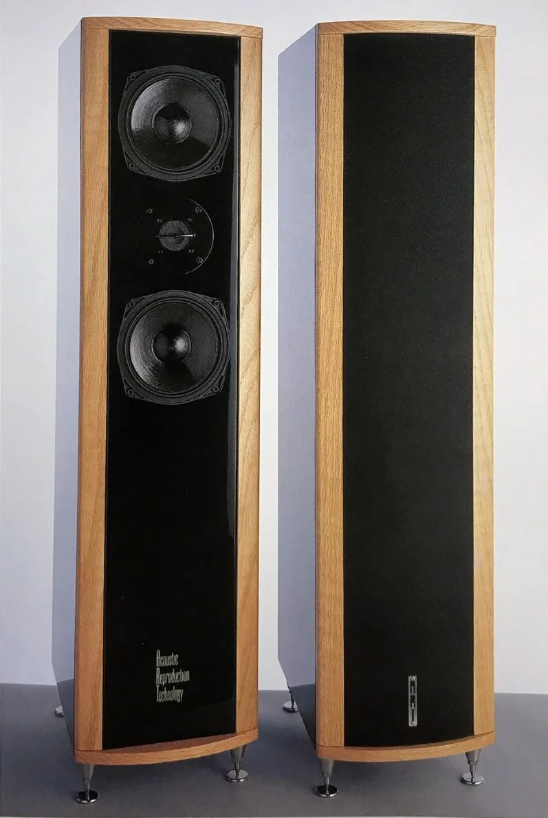 Pair of tall, vintage-style wooden speakers with black front panels, one with its grille removed revealing two large speakers and a smaller dial in the middle.
