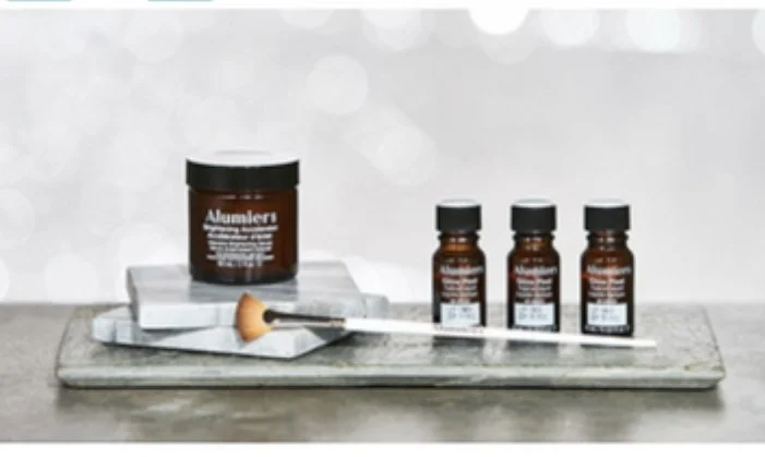 Set of alumaeri plastic and liquid containers on marble tray, with a makeup brush and tissue paper, on a grey surface with blurry background.