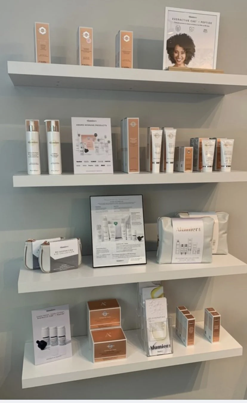 Display of skincare products and promotional materials on white wall shelves in a retail space. The shelves contain bottles, boxes, and informational signs related to skincare and beauty. There is a framed certificate or award on the top right shelf.