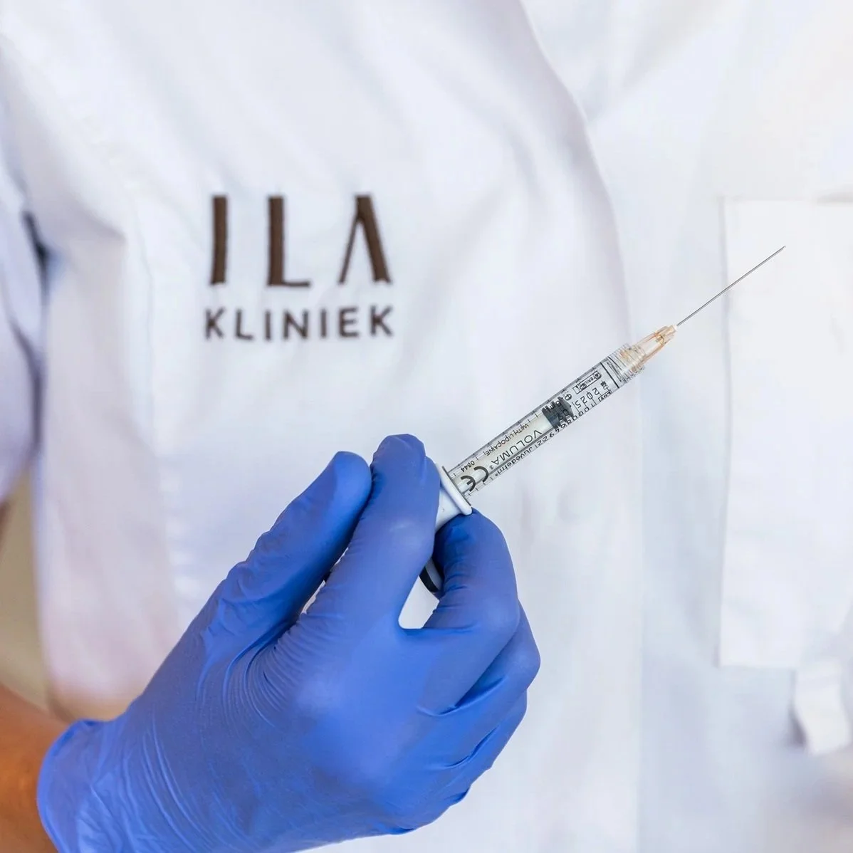 Afbeelding voor bij het blogartikel over botuline toxine voor mannen. Op de afbeelding houdt een cosmetisch arts KNMG een injectie vast, terwijl ze blauwe handschoenen draagt en een wit jasje met daarop ILA Kliniek.