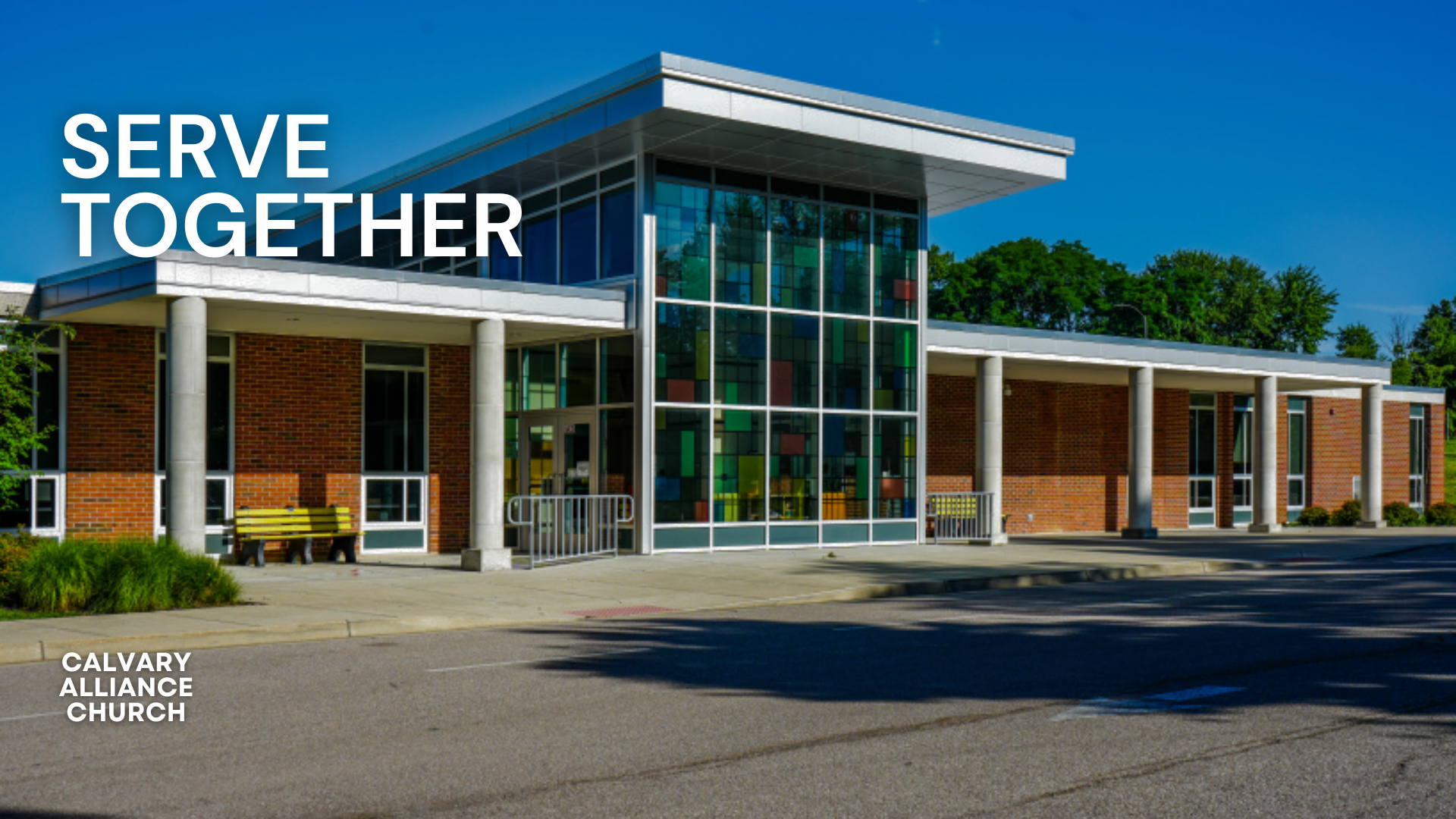 Exterior of Calvary Alliance Church building with glass entrance and red brick walls, under a clear blue sky with trees in the background.