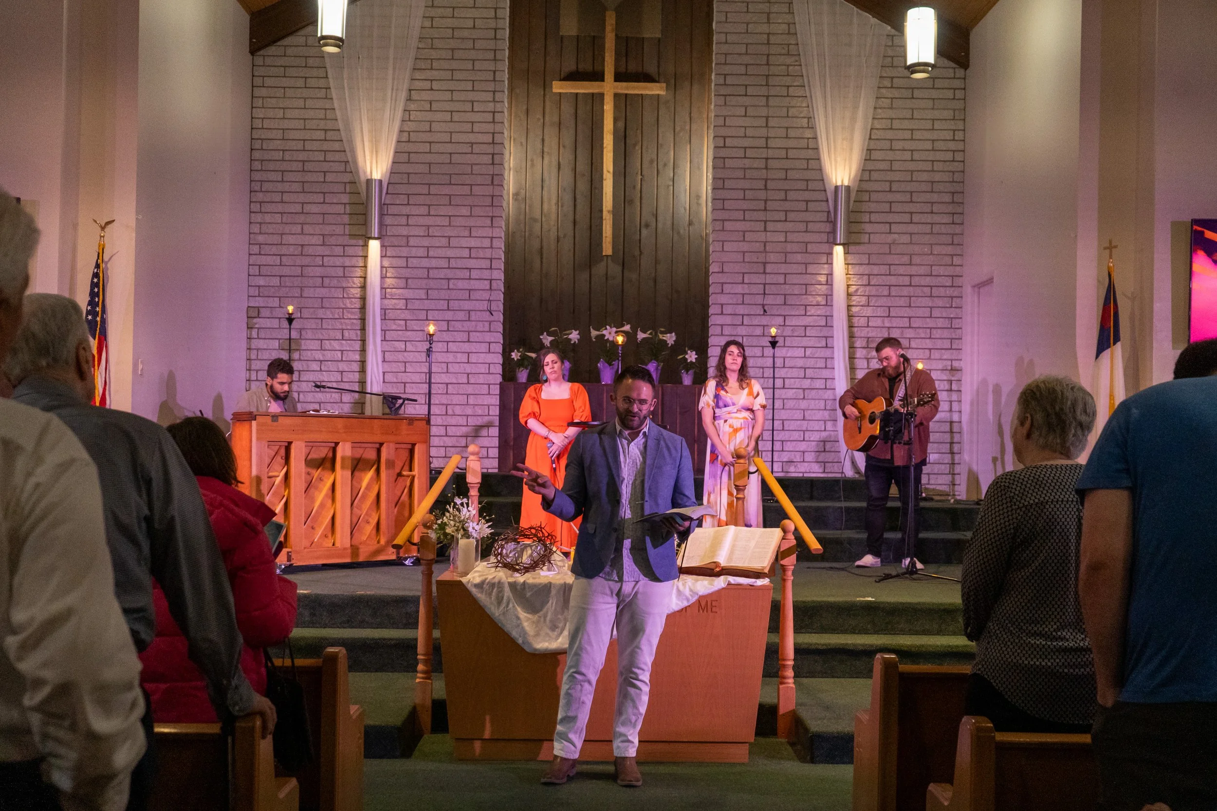 Church service with pastor preaching and worship team on stage, congregation seated.