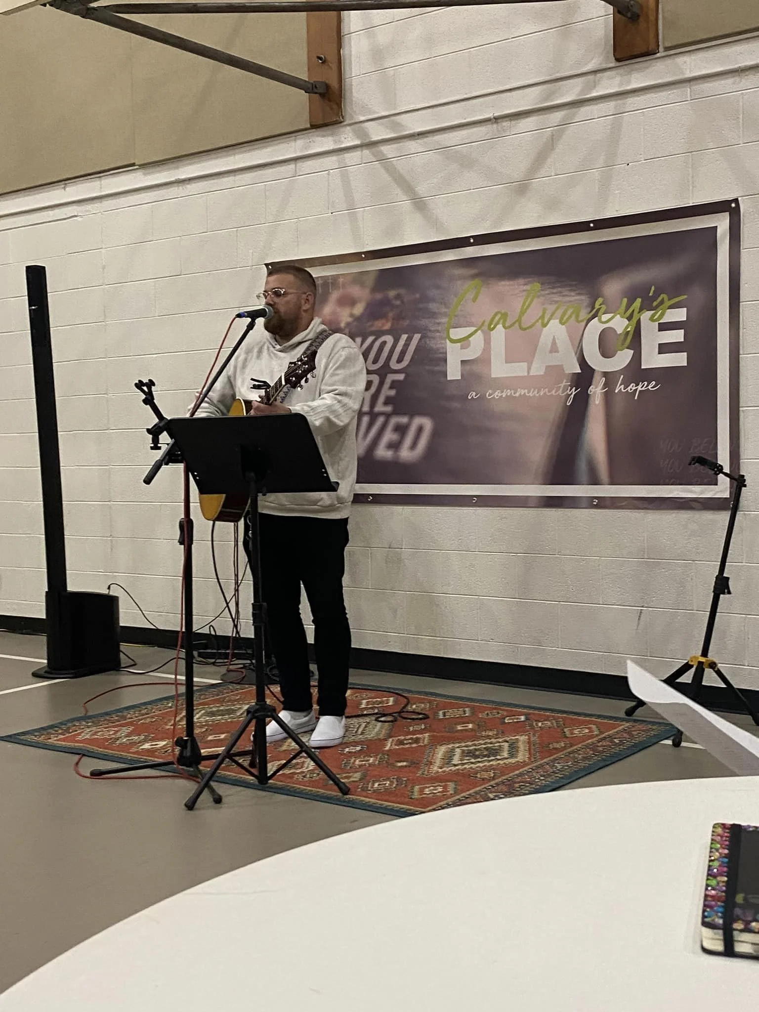 Person singing and playing guitar on stage in a church setting, with 'Calvary's Place' banner and microphone stand.