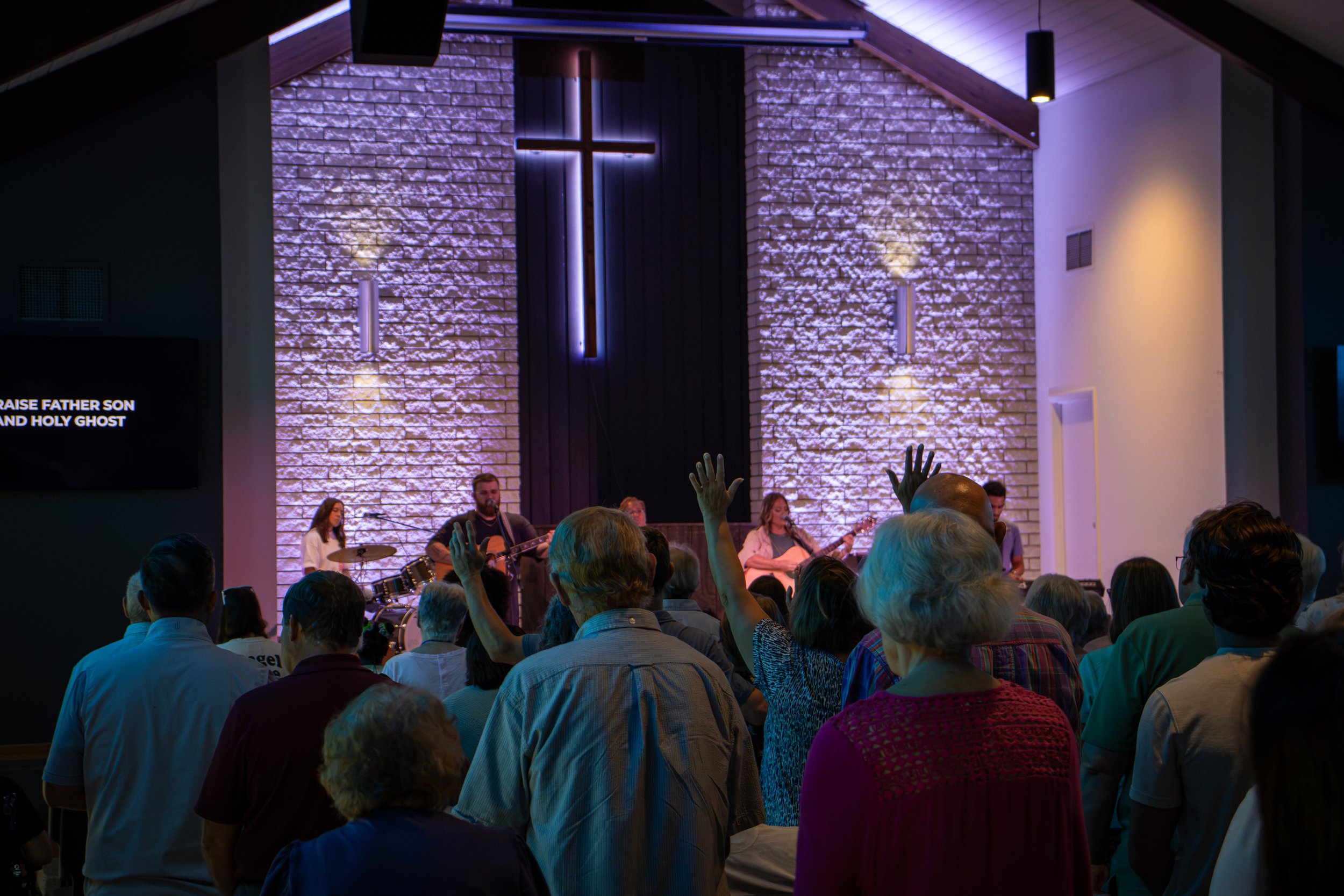 Church service with pastor preaching and worship team on stage, congregation seated.
