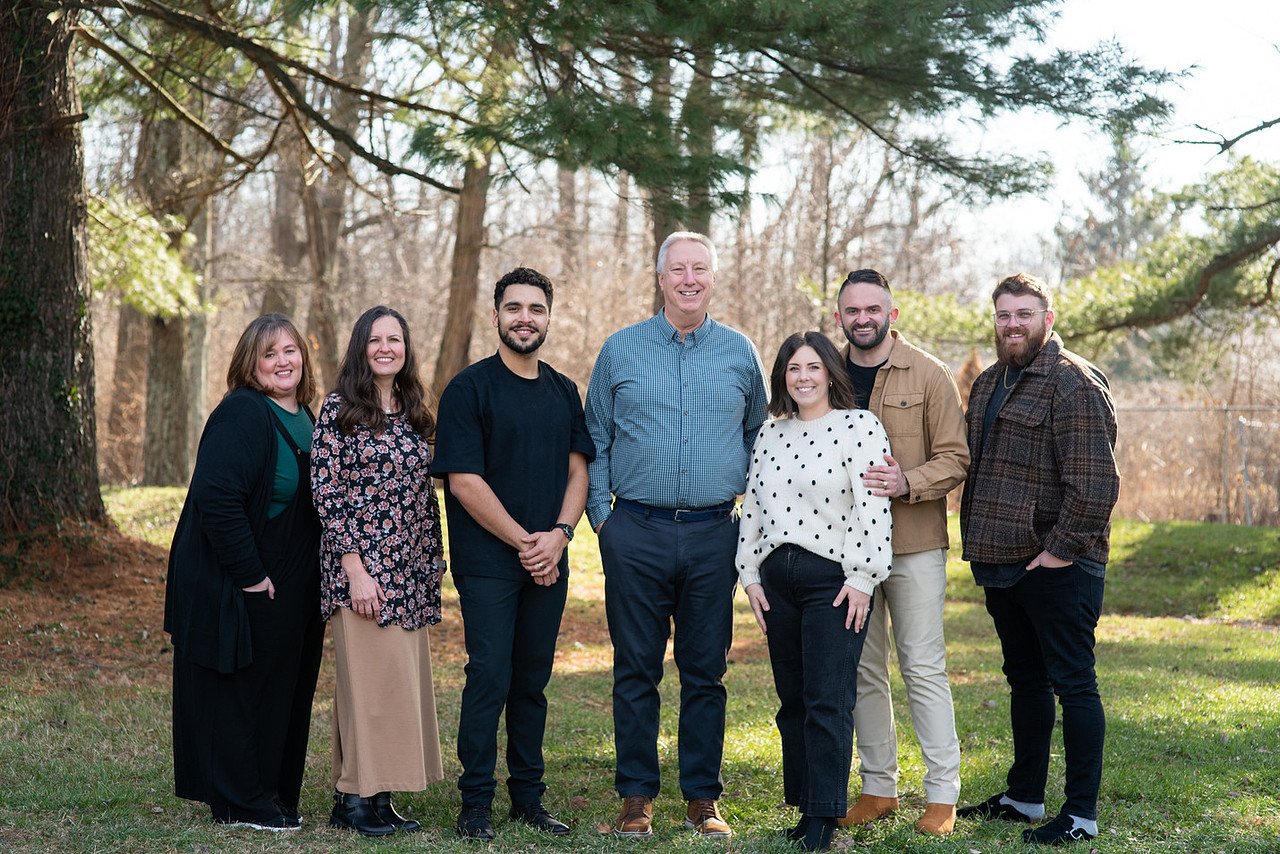 Group of seven people standing outdoors in a park, smiling at the camera.