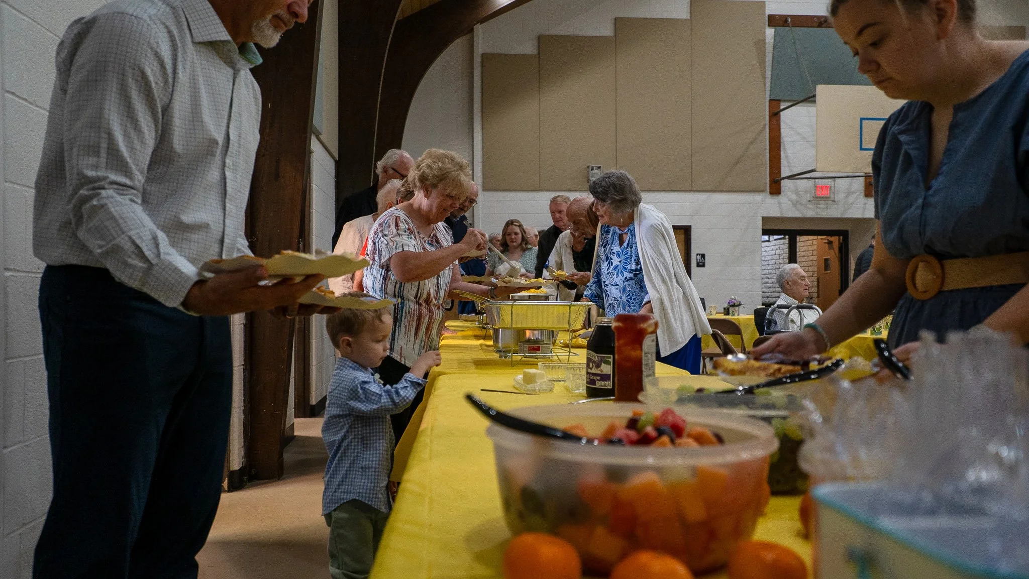 Volunteers organizing and distributing food bags at a community event in a room labeled for 1st-5th grade.
