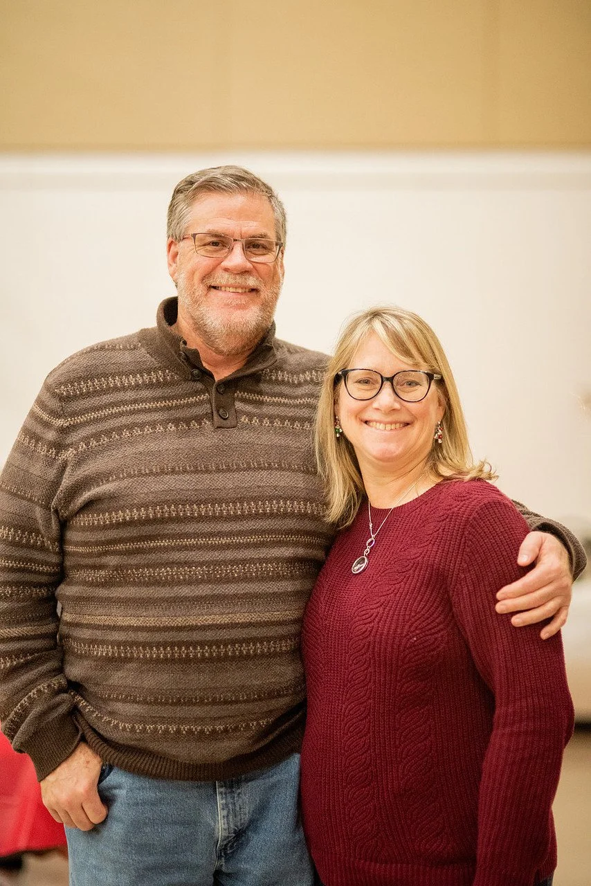 A man and a woman standing close together, smiling, with the man's arm around the woman's shoulder.