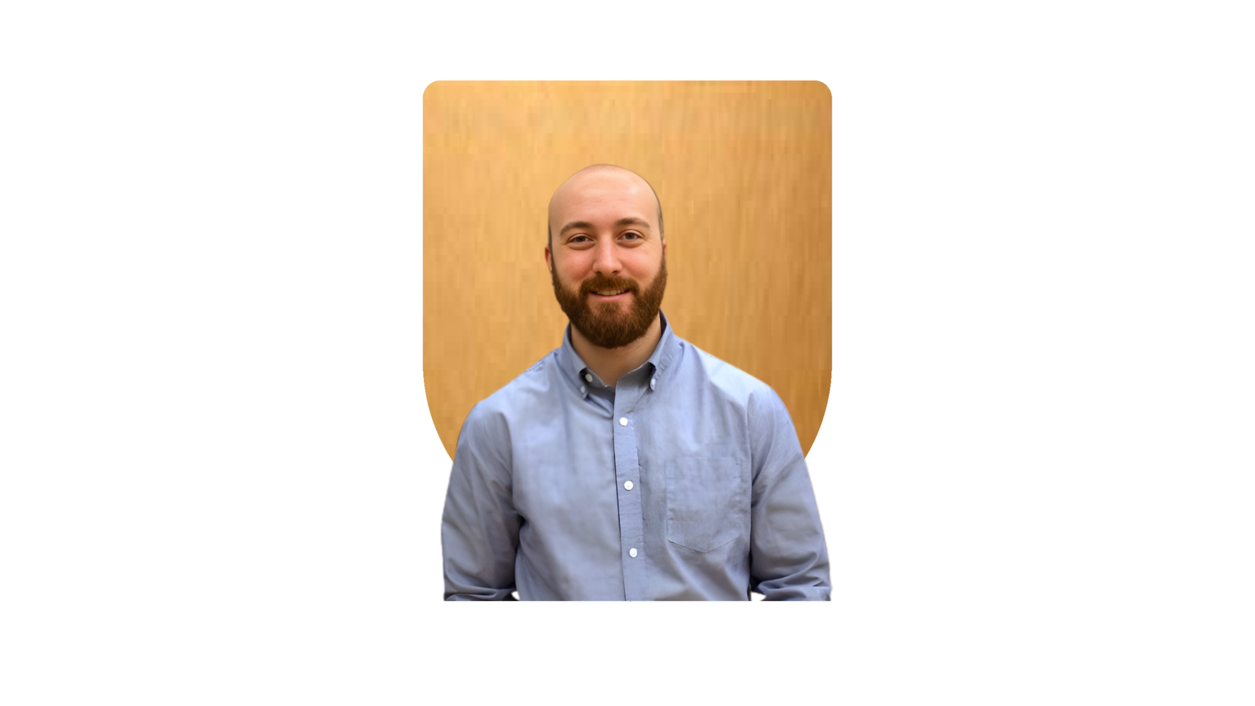 A portrait of a bearded man with a shaved head, wearing a light blue button-up shirt, smiling, with a wooden background.
