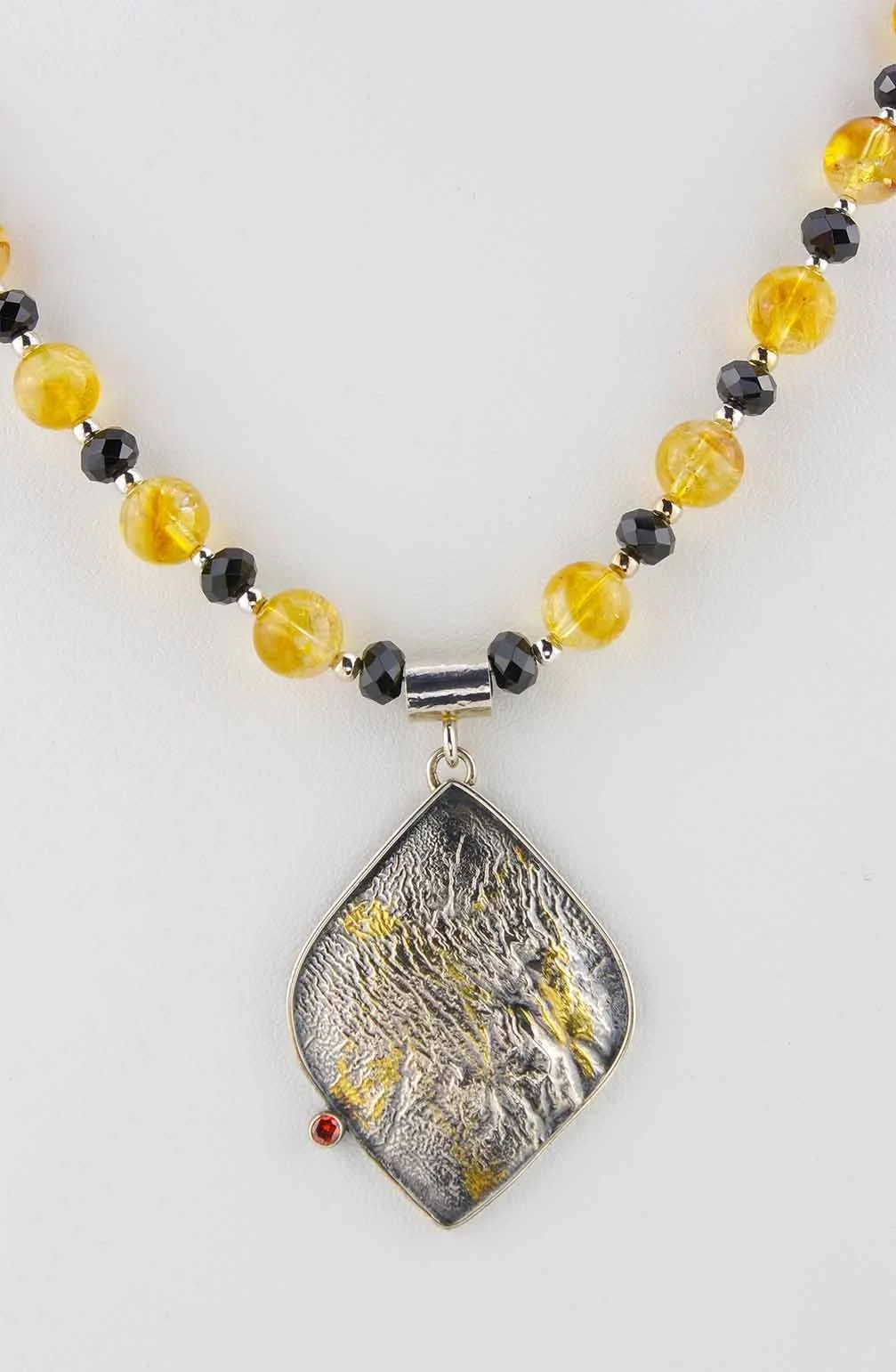 Detail of reticulated silver pendant strung with citrine and spinel rondelle beads.
