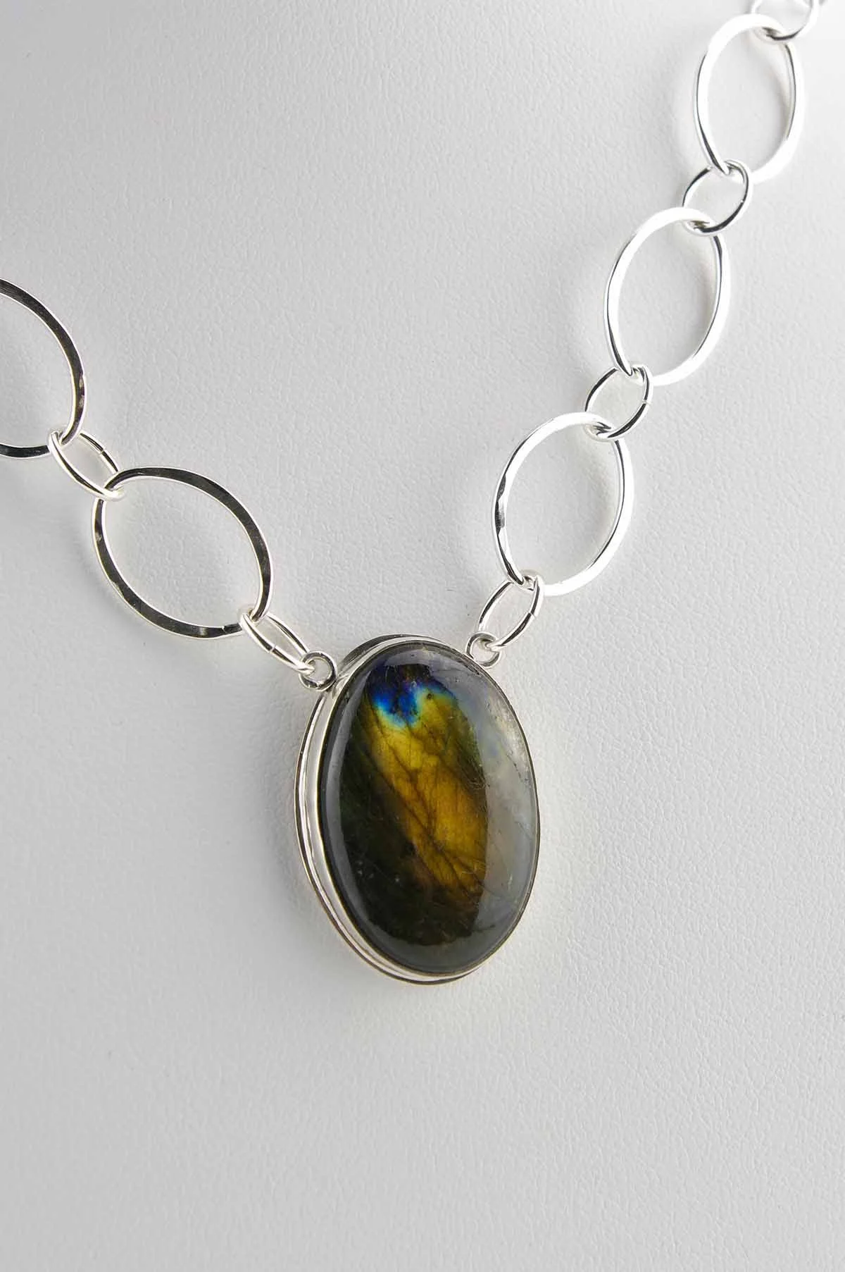 Oval orange labradorite in vertical setting on a hand-fabricate oval sterling silver chain. Detail view of the stone.