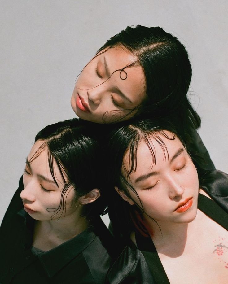Three women with wet hair and closed eyes, forming a composition with their heads close together against a plain background.