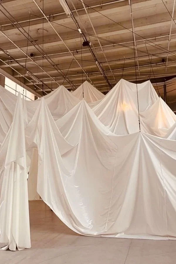 Indoor installation with white fabric draped to create mountain-like peaks, suspended from the ceiling in an industrial space.