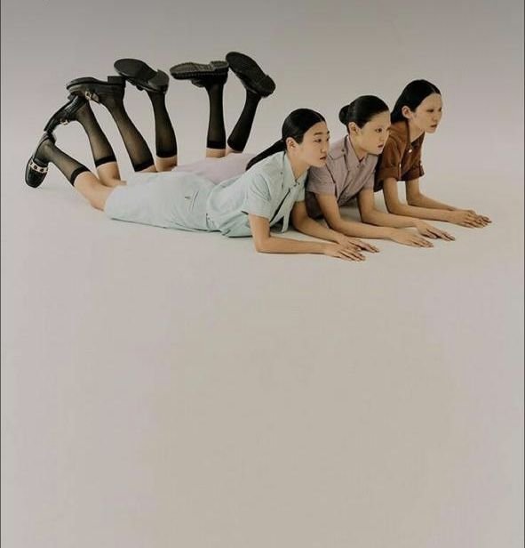 Three women lying on their stomachs, with their legs elevated and bent at the knees, wearing different colored uniforms, against a plain light background