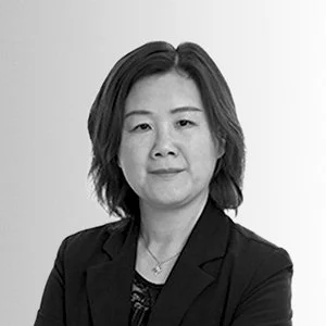 Black and white portrait of a woman with shoulder-length hair wearing a blazer and a necklace, looking at the camera.