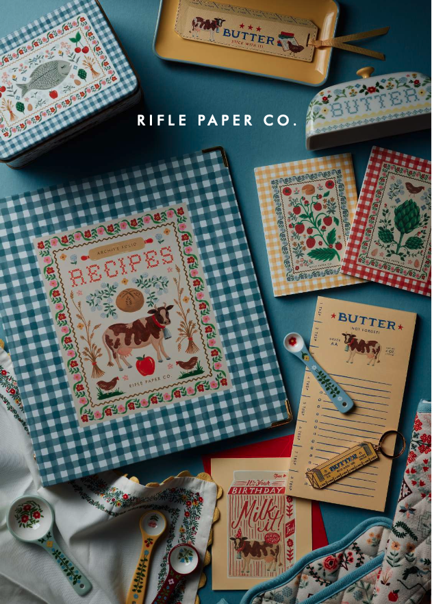 Vintage farm-themed decorative plates with animals like cow, goat, duck, and hen around the edges, festive holiday and home messages, notepad, a small scrapbook, green patterned cloth, and a small heart-shaped object, all arranged on a beige fabric background.