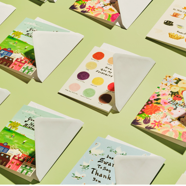 Various colorful greeting cards with floral, scenic, and thank you messages, displayed on a light green surface.