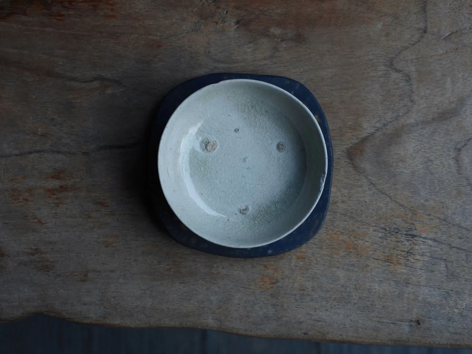 Overhead view showing the inner surface of a glossy Vietnamese vessel resting atop a Japanese plate with matte, mineral-rich glaze