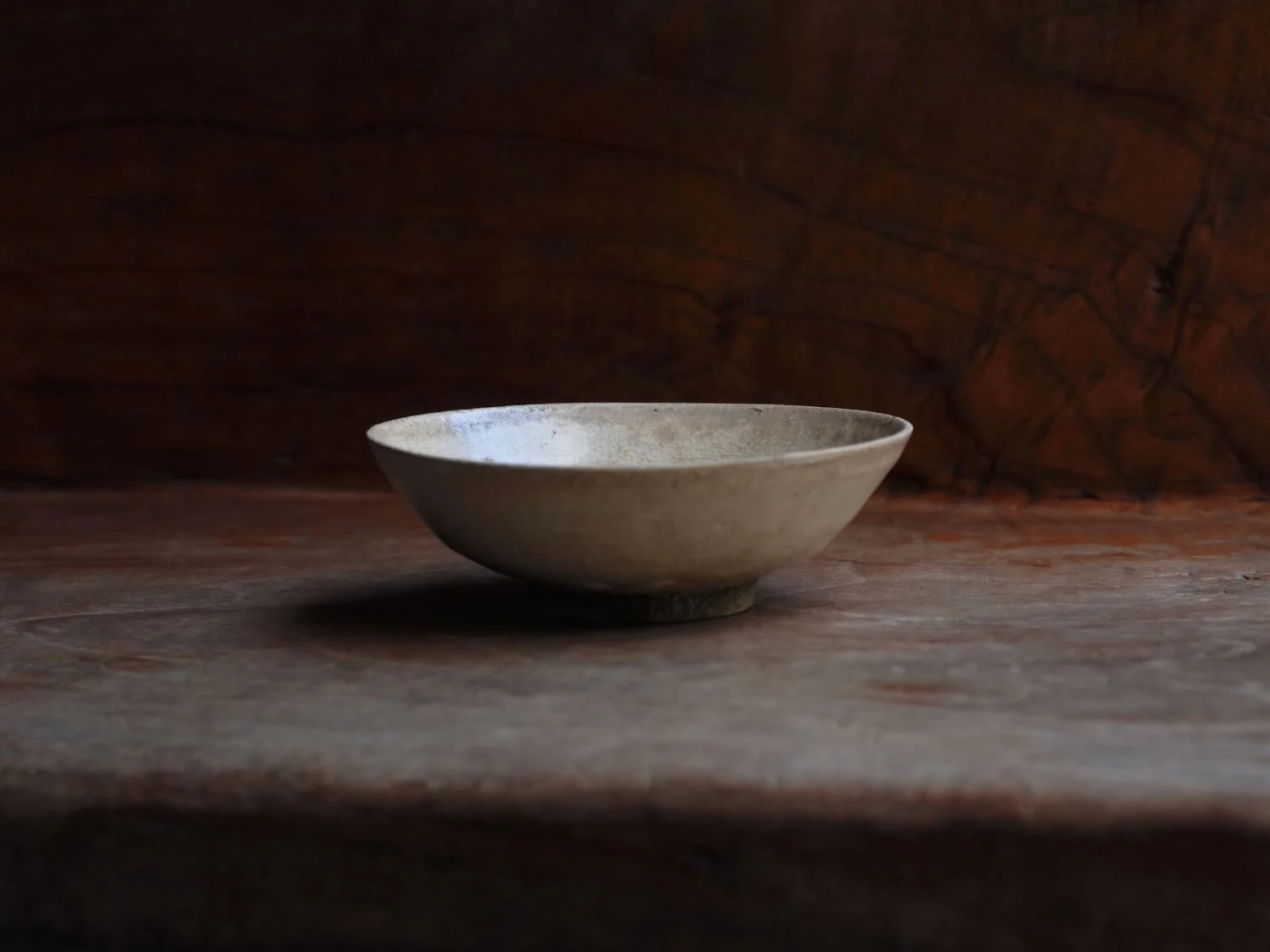 Low-angle side view of a delicate ceramic plate from Vietnam dating back Le Period, highlighting its shallow bowl form and elegant, light-reflecting glaze