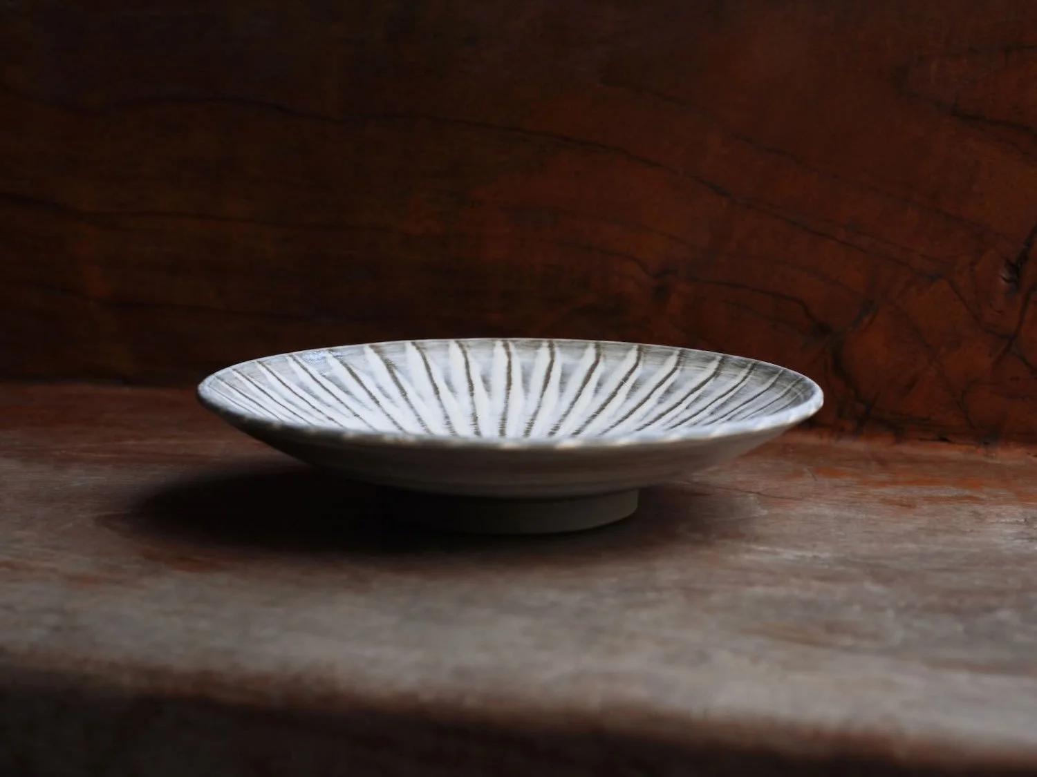 Onta ware plate featuring hand-carved lines displayed on a rustic wooden surface