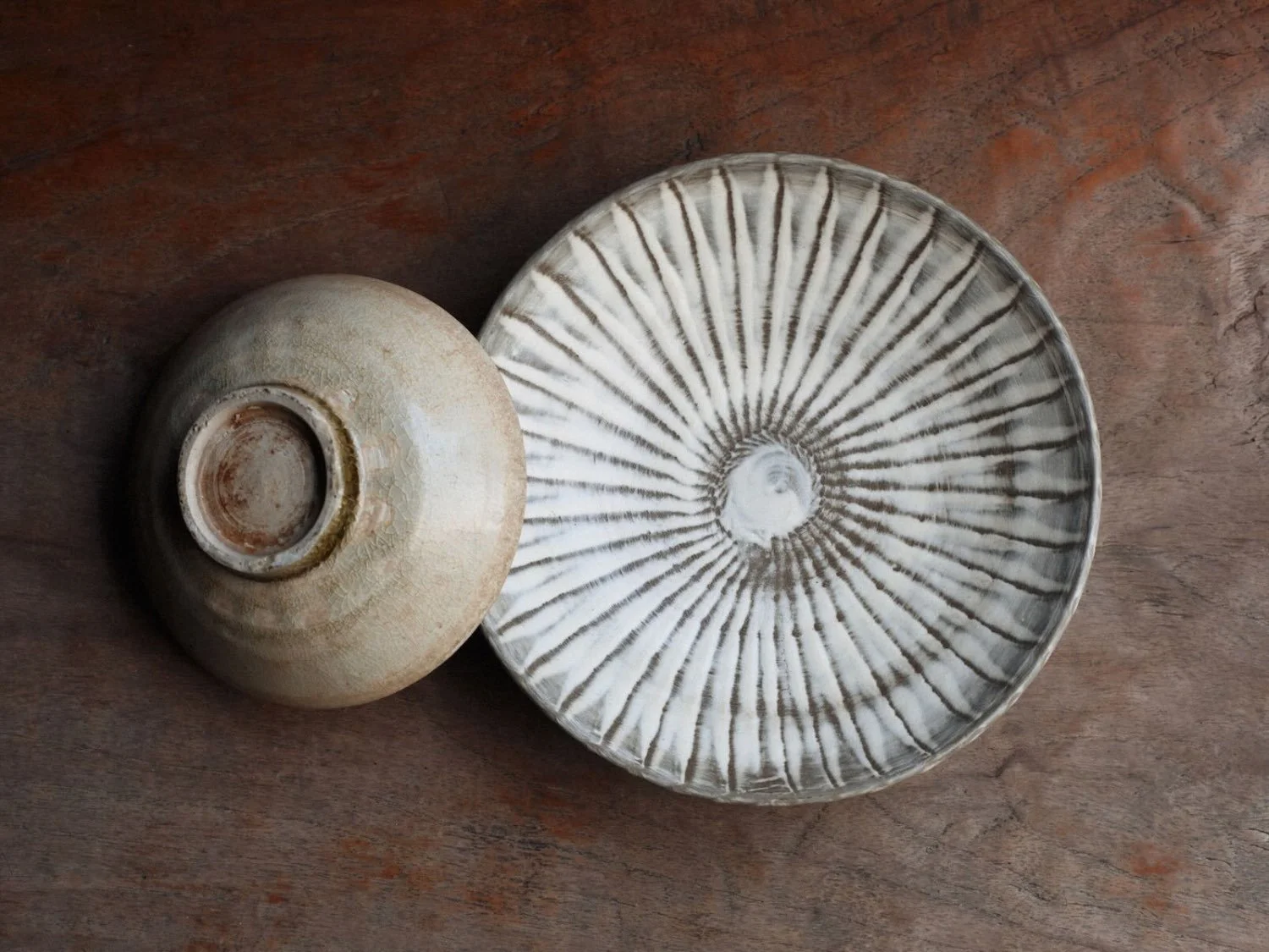 Stacked set of a plate and small cup seen from above and below, showcasing both the decorative front and footed base of each ceramic piece
