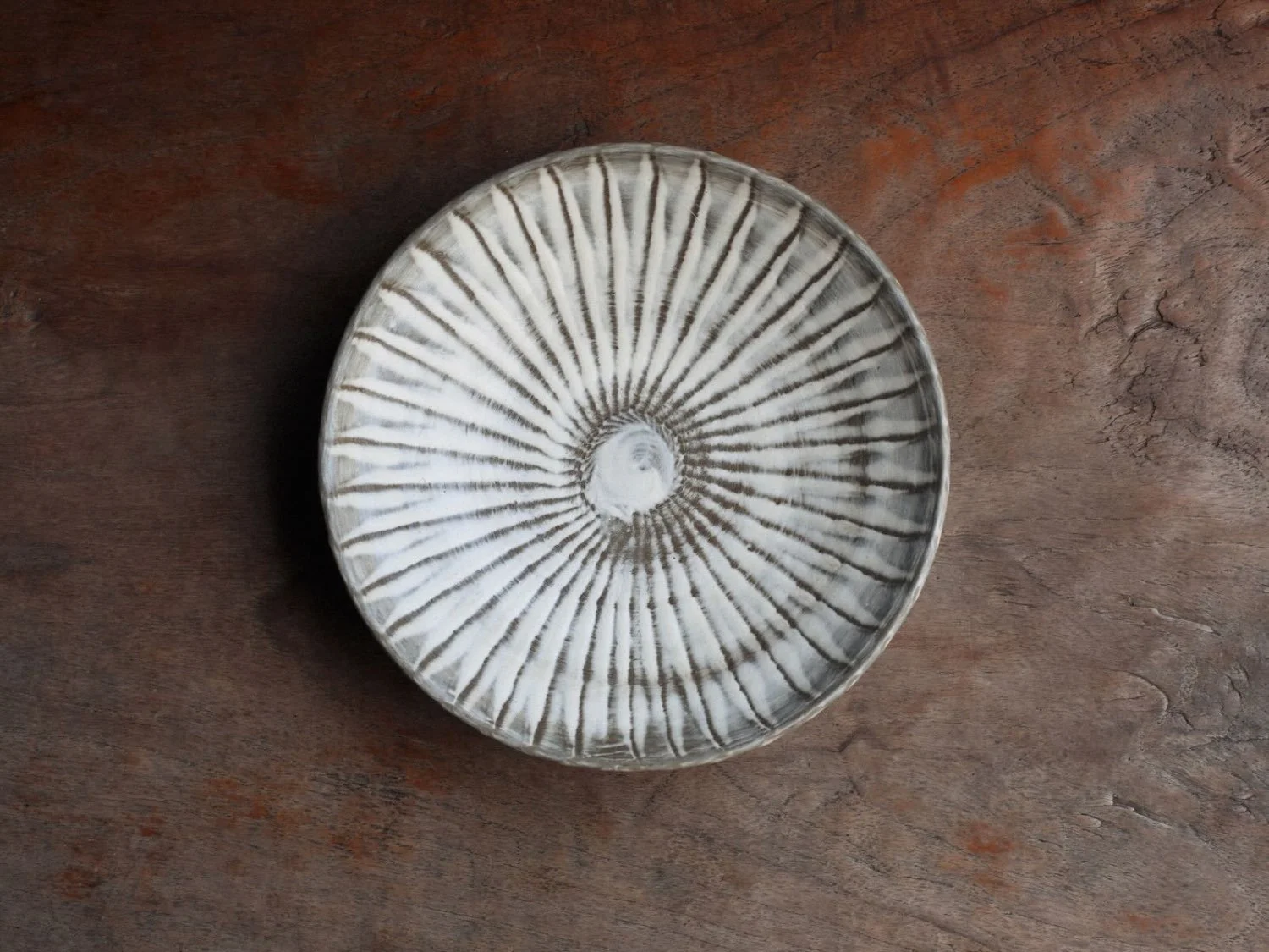 Top-down view of a hand-carved plate from Onta village in Japan, with distinct radiating brush marks and soft, white-green glaze
