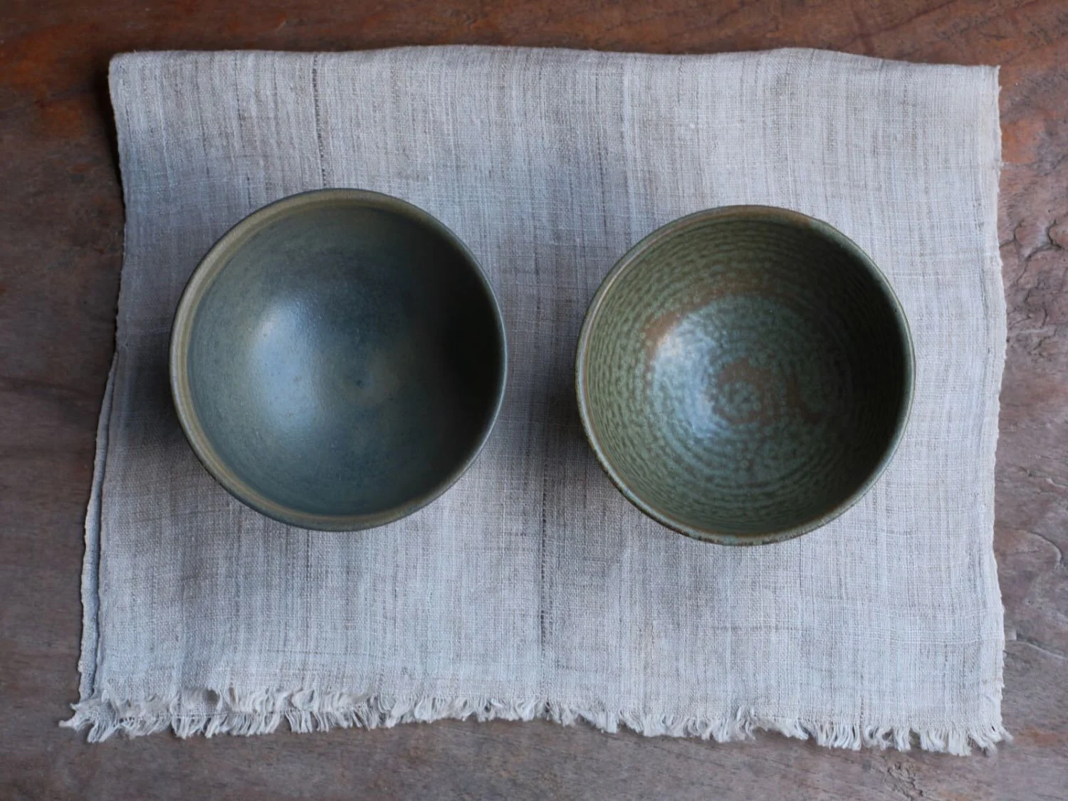Overhead view of two Japanese ceramic bowls showing their interiors, placed on a frayed-edge linen cloth