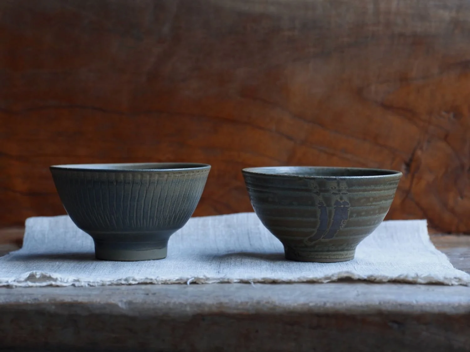 Pair of handmade Japanese ceramic bowls with subtle glazed patterns, displayed side by side on a linen cloth