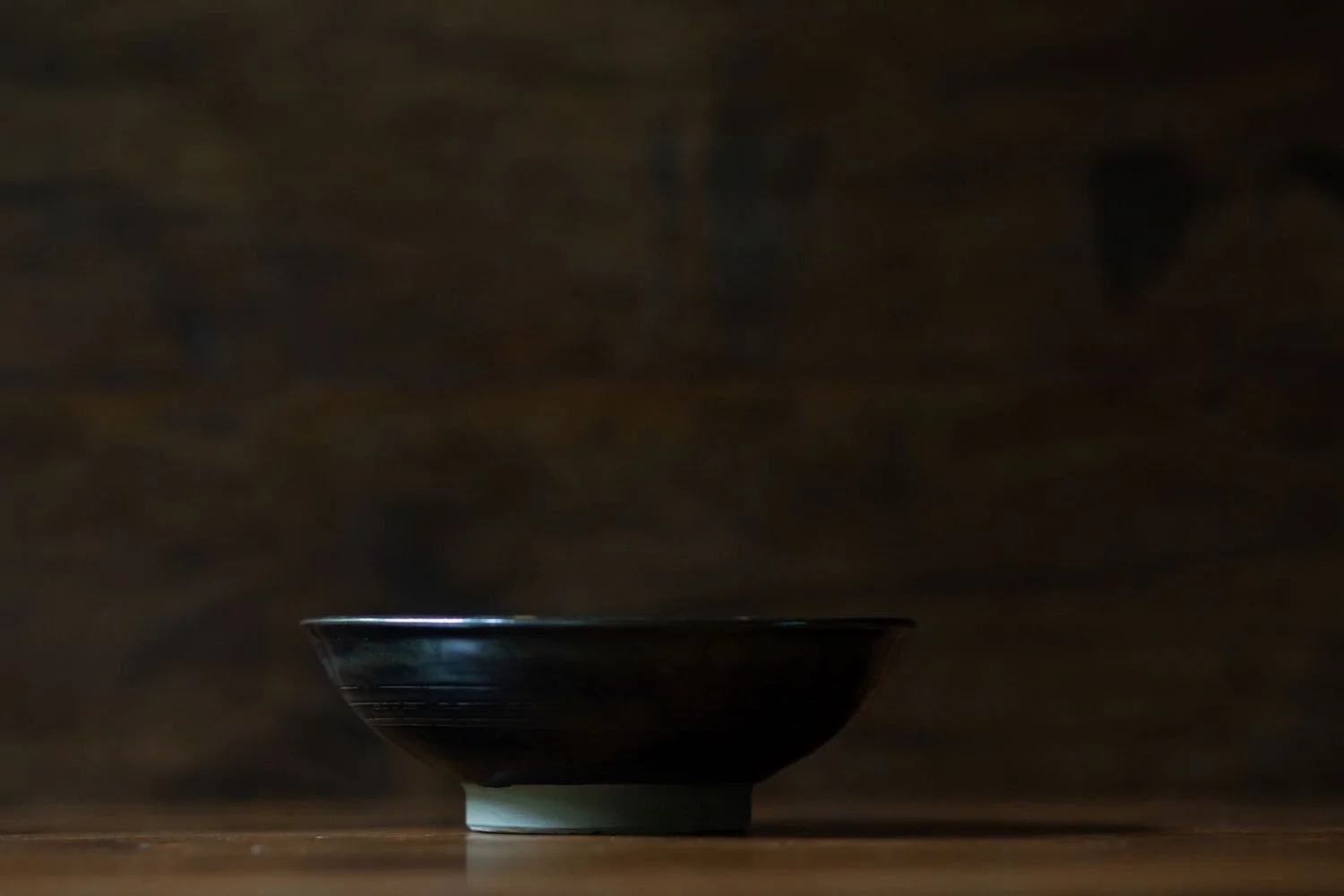 Side profile of the ceramic plate showing its curved silhouette and elevated foot, photographed against a dark wood backdrop.