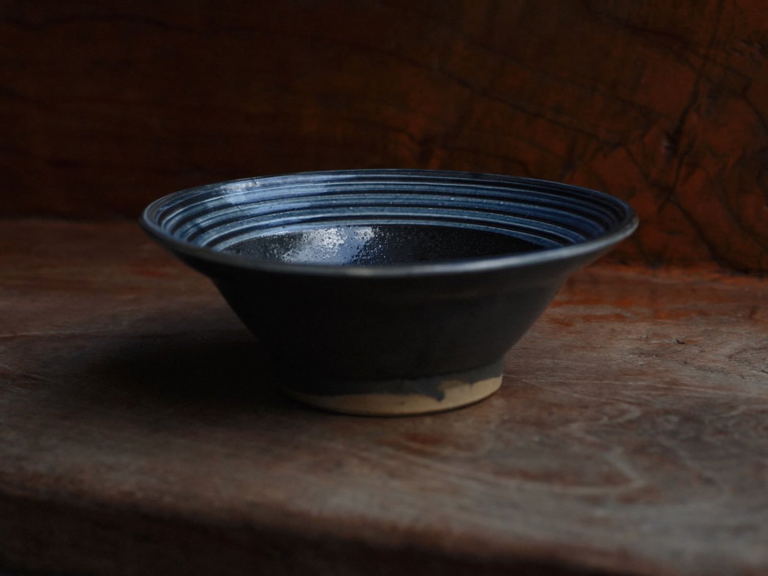 Dark blue ceramic bowl with ringed rim on a rustic wooden table.
