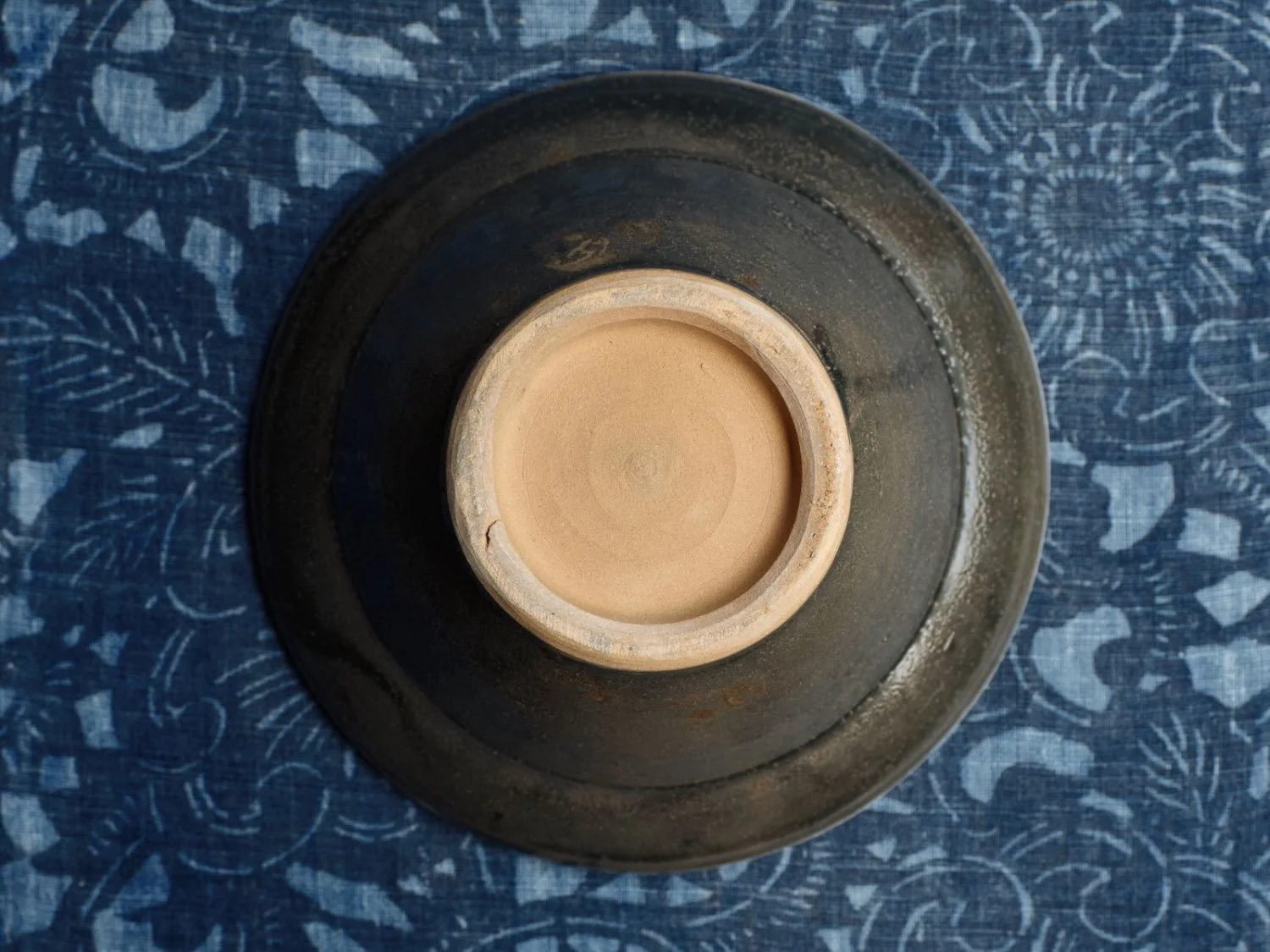 Underside of a dark ceramic bowl with unglazed clay foot, on indigo katazome cloth from Meiji period.