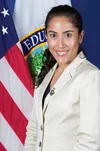 Portrait of a woman in professional attire standing in front of American and state flags.