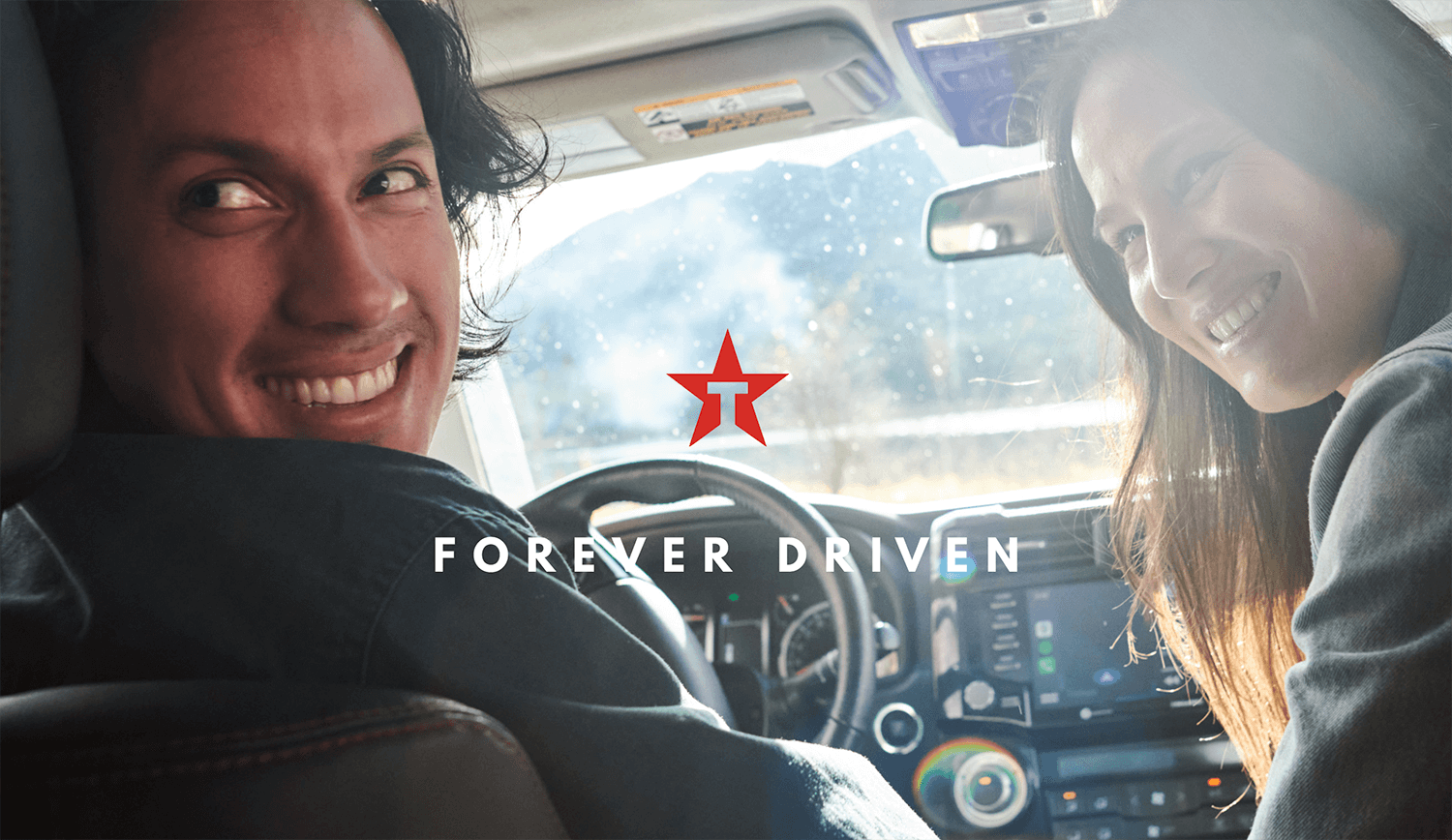 Two friends in a vehicle look toward the backseat and smile.