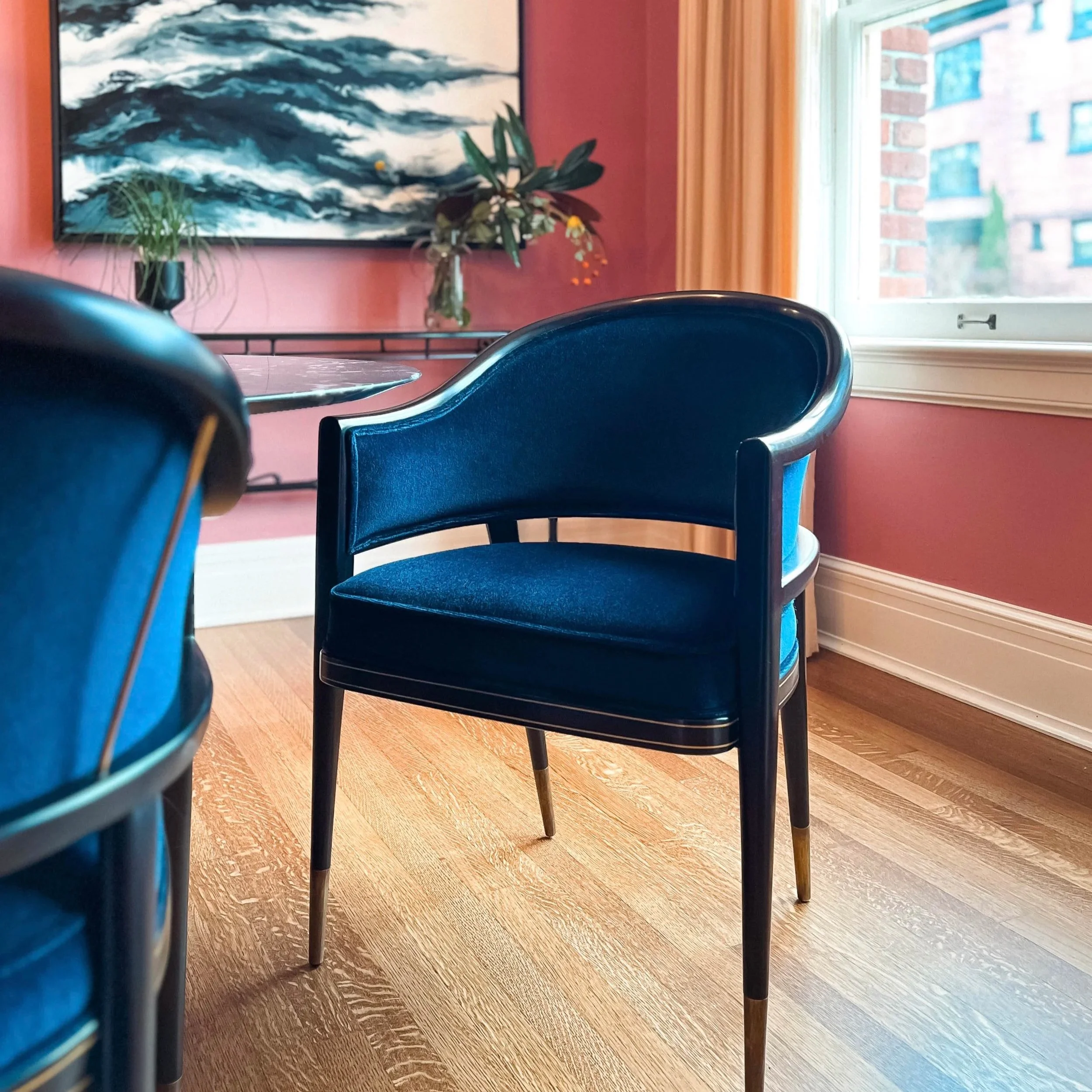 Two blue velvet dining chairs seen in a pink room.