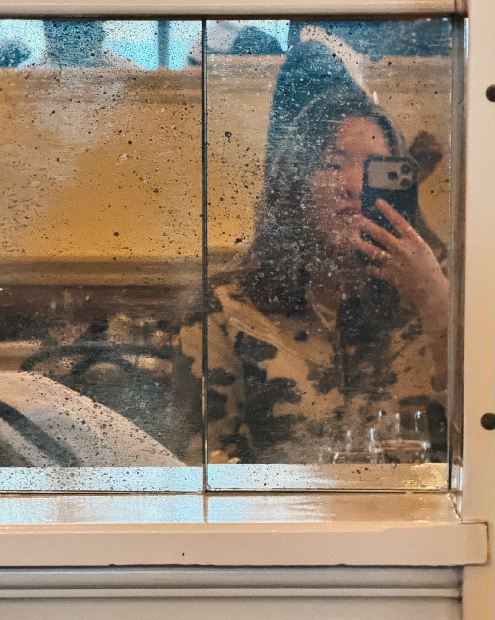An artistic photo reflecting a woman taking a photo with her camera in a room with beige or light-colored interior walls.