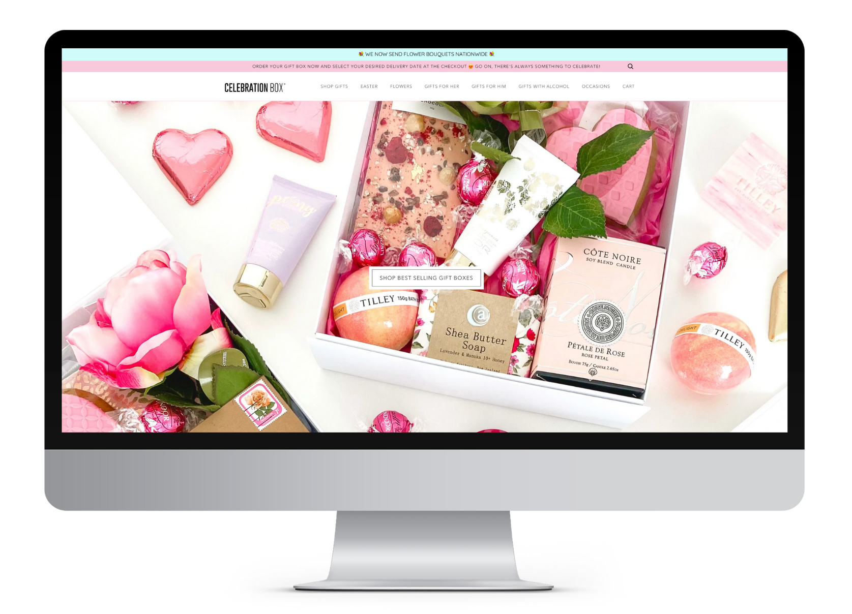 Box of pink and floral-themed gifts and chocolates, including a soap, a rose-shaped candle, chocolates, and a pink rose, arranged on a white surface.
