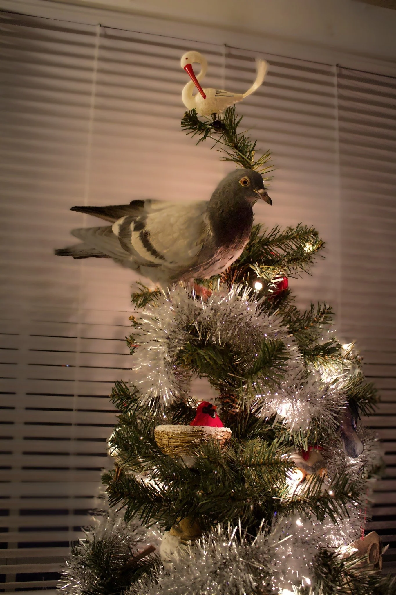 Decorated Christmas tree with a bird perched on top, featuring ornaments, tinsel, and string lights.