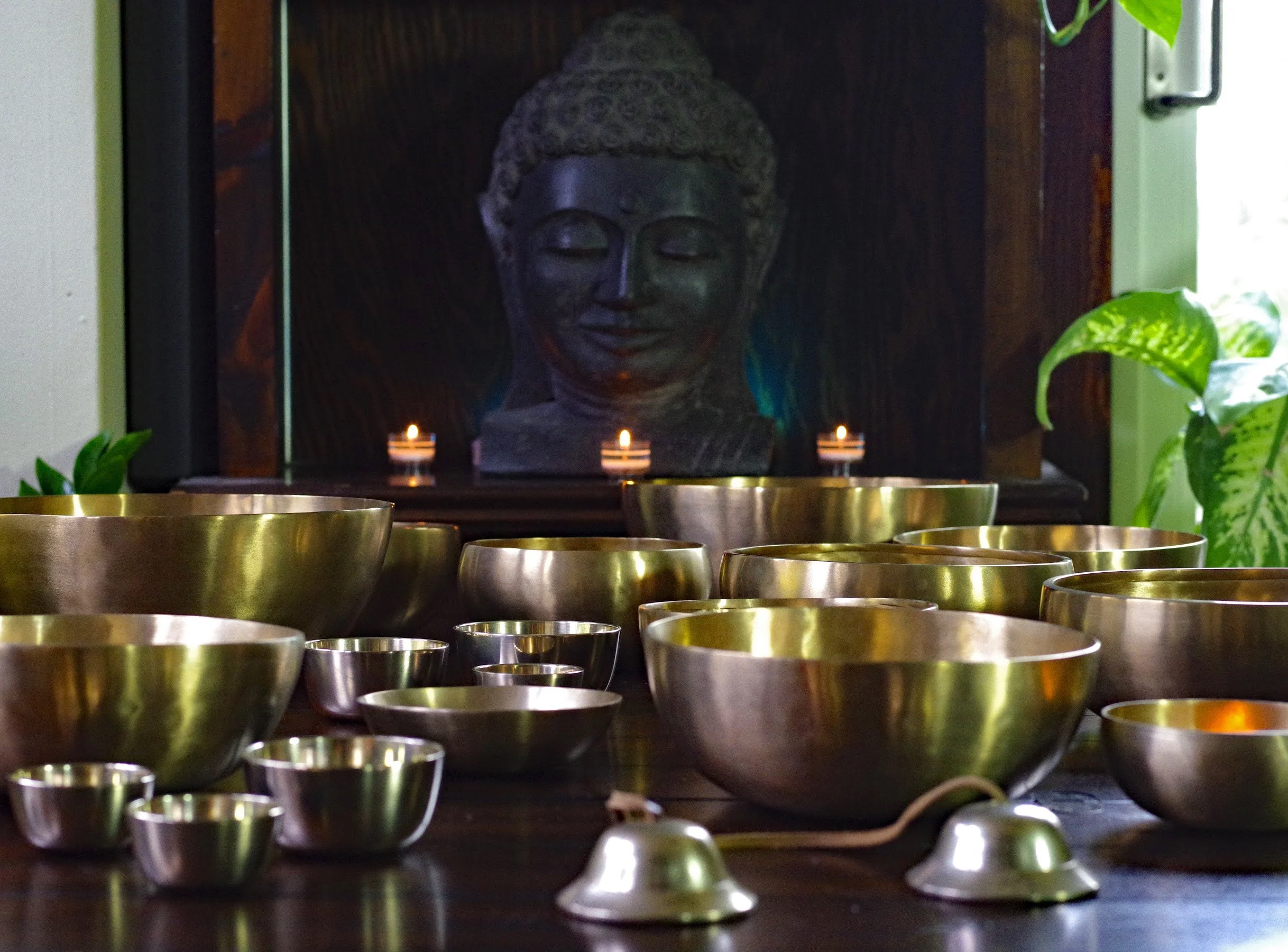 Tibetan singing bowls arranged in front of a Buddha statue with candles for a sound healing session