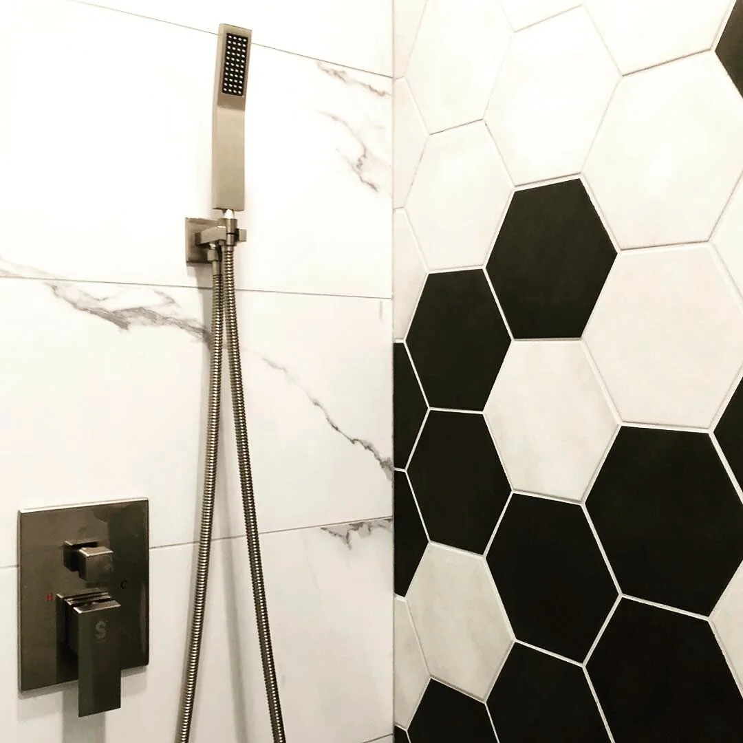 This custom hexagon-tiled shower was a fun one for our team! Complete with a sleek shower head and inset shelving #customshower #hexagontiles #blackandwhite #yycrenos #yycshowers