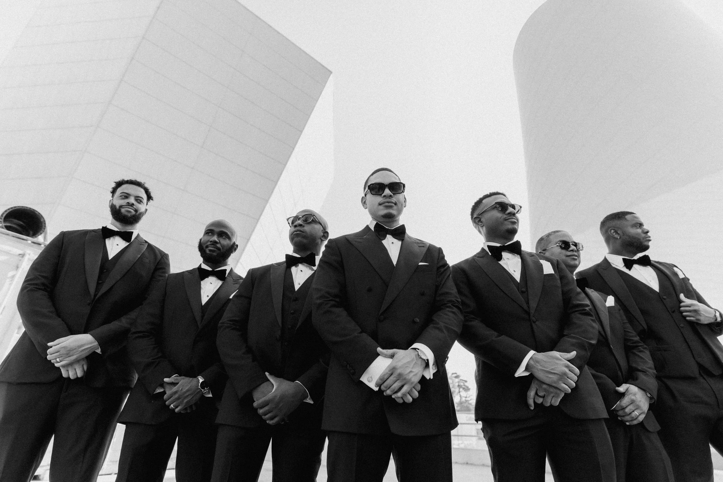 Groomsmen standing in formation outdoors against modern architectural buildings.