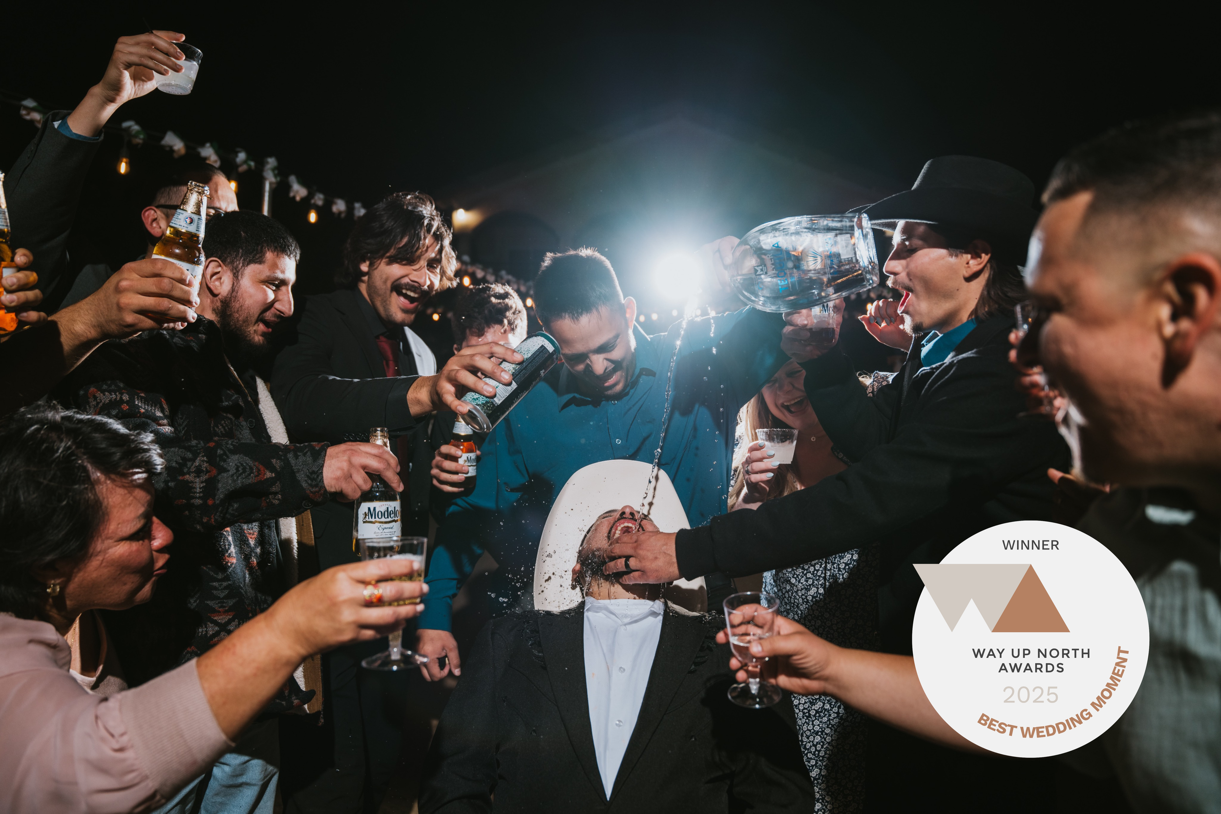 A group of people at a celebration, pouring drinks and celebrating as a man in the center is crowned as a winner at the 2025 Way Up North Awards event.