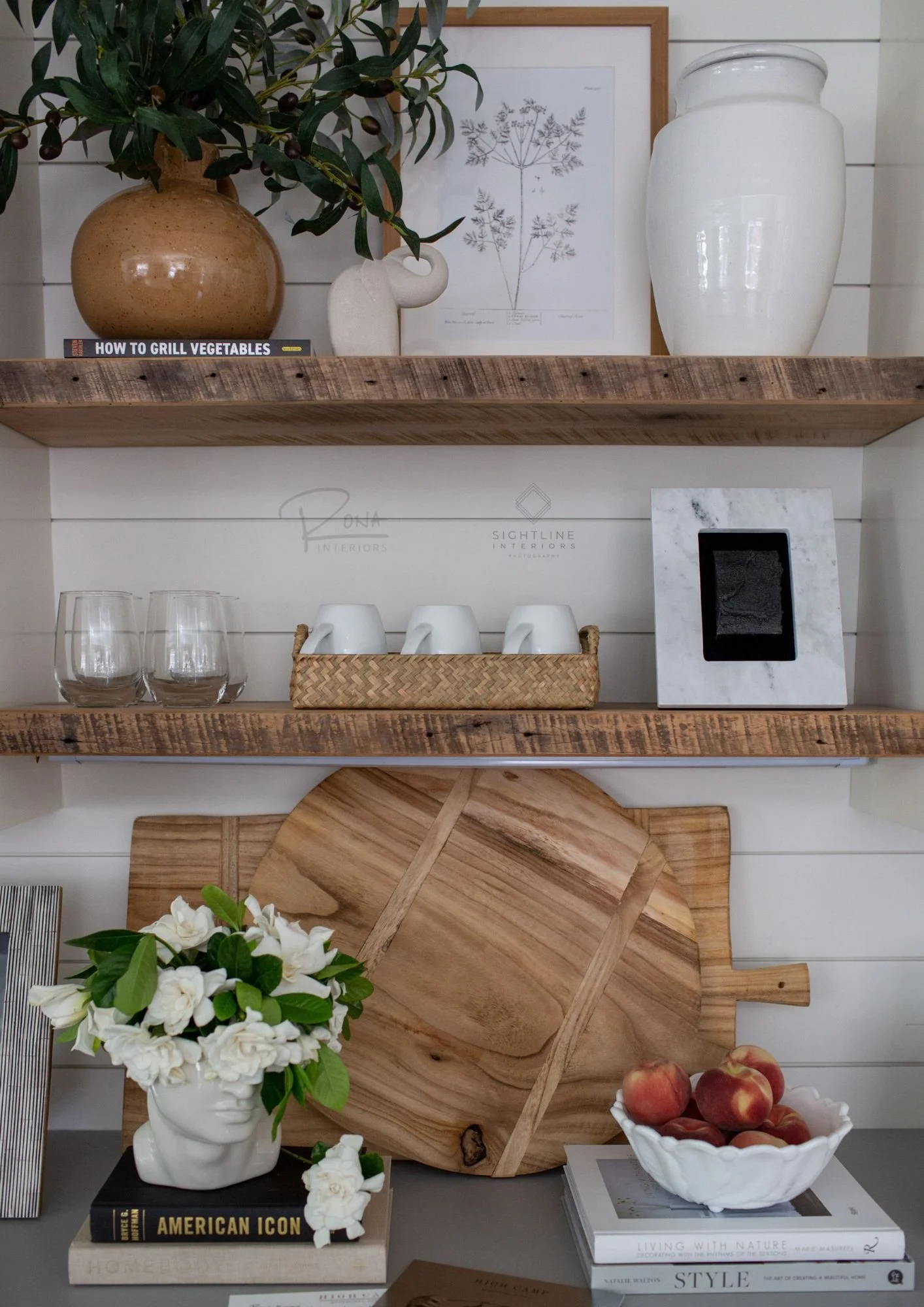 Rustic kitchen shelf decor with wooden shelves, ceramic and wooden vases, cutting boards, books, and bowls of peaches and flowers.