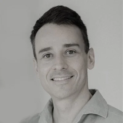 Black and white portrait of a smiling man with short dark hair, wearing a collared shirt.