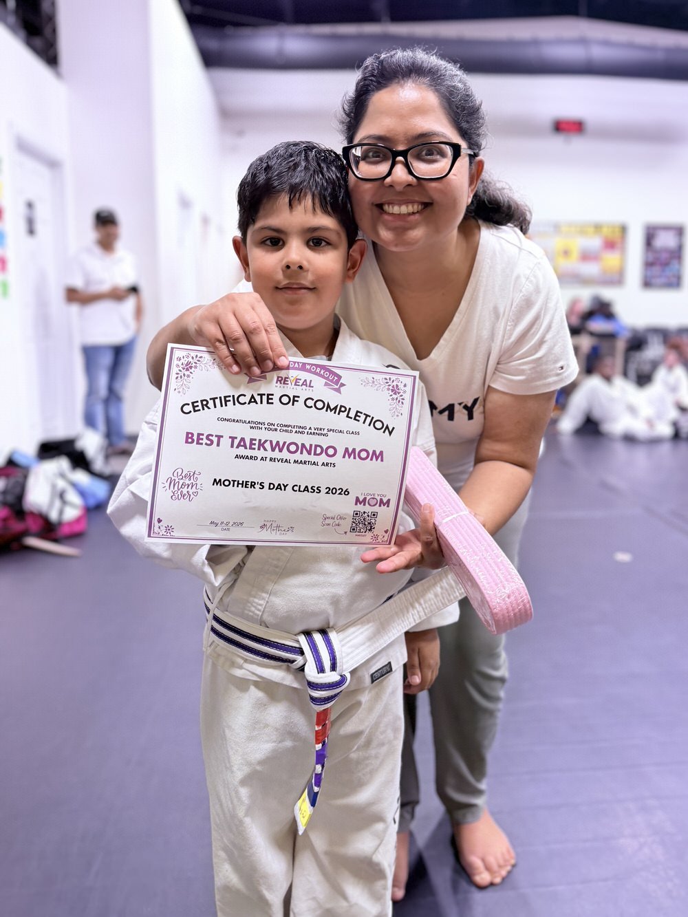 Mother hugging her son after completing Reveal Martial Arts Mother's Day class and receiving a pink belt and certificate.
