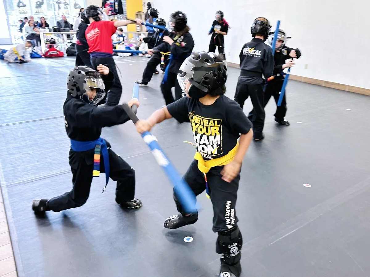 Group of kids sparring with sticks in a martial arts class at Reveal Martial Arts.