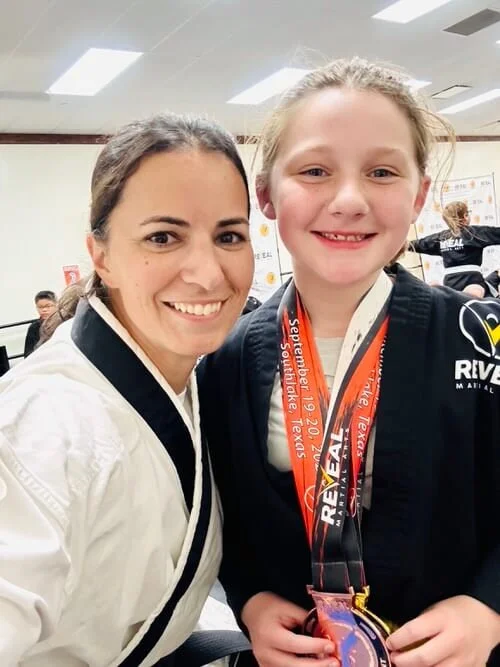 Confident girl in martial arts karate class showing of tournament medals to her instructor.