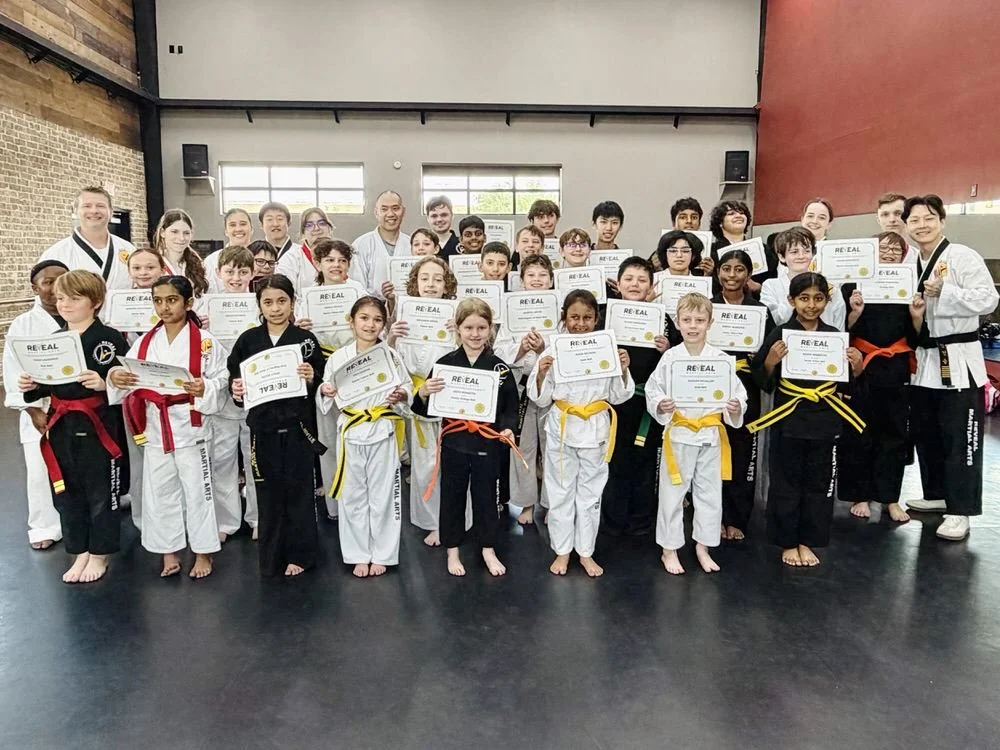 Kids and instructors at Reveal Martial Arts posing with belt promotion certificates after martial arts testing in Texas.